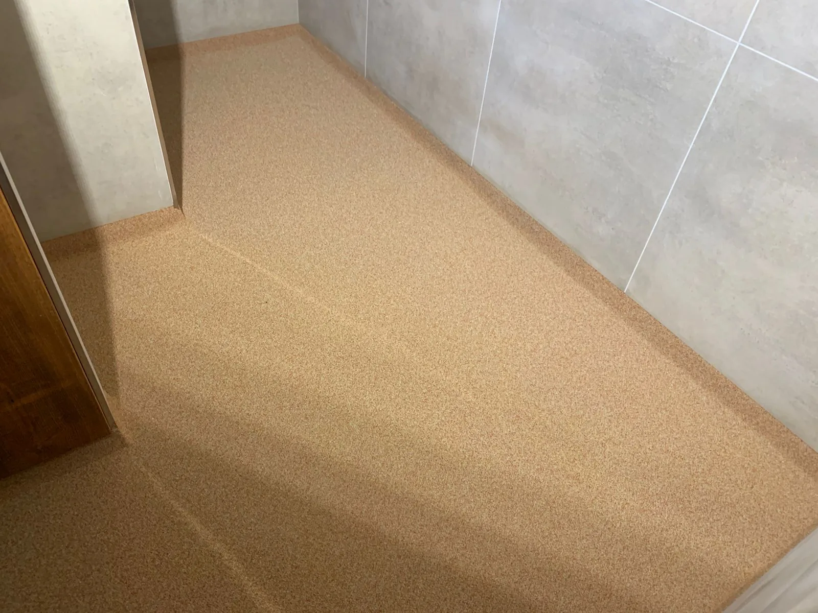 Beige kwartsvloer met opstaande kim tegen een grijze tegelwand
