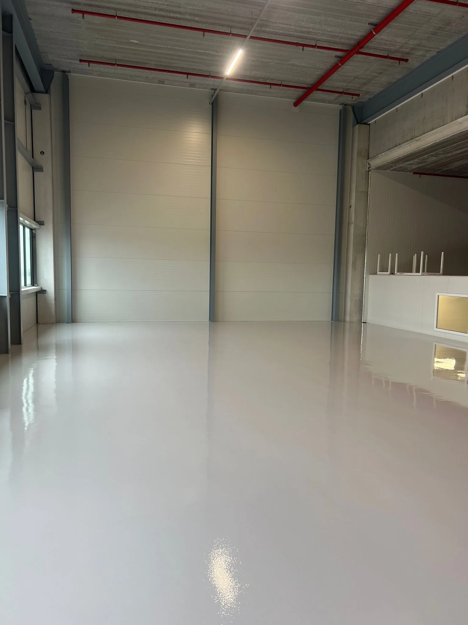 Naadloze grijze epoxy gietvloer in een nieuwe bedrijfshal met wandpanelen en overheaddeur