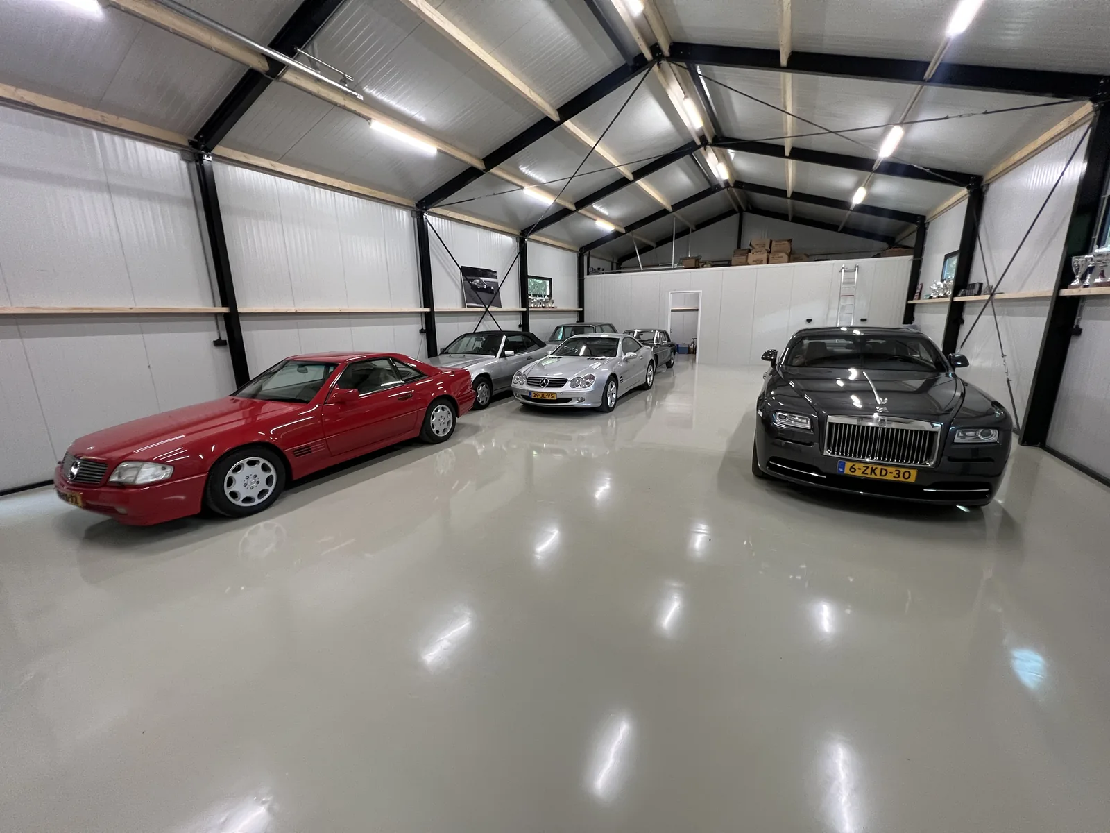 Lichte epoxy gietvloer in een garage met klassieke sportwagens onder een houten kapconstructie
