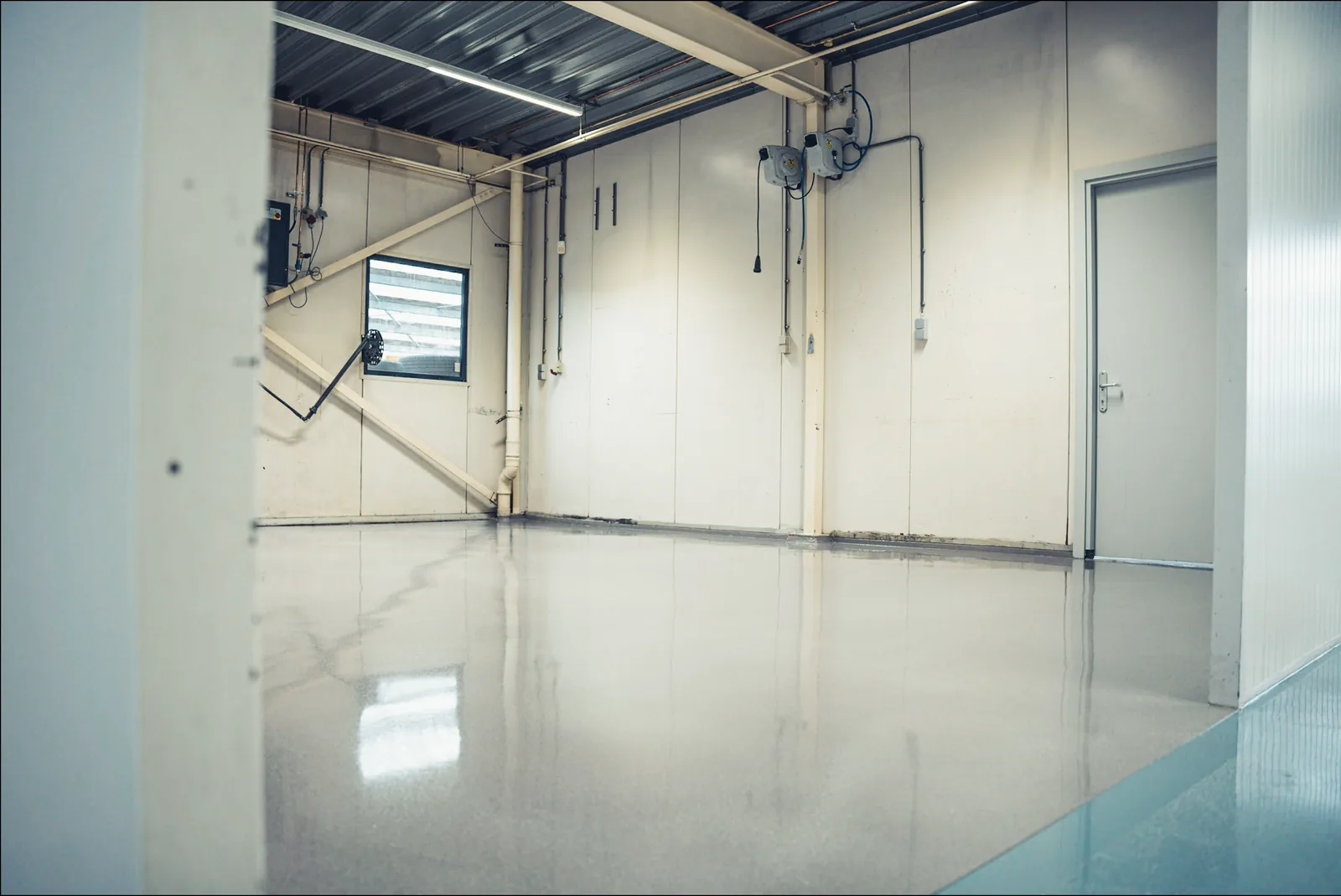 Grijze epoxy coating in een bedrijfsruimte met leidingwerk en witte wanden