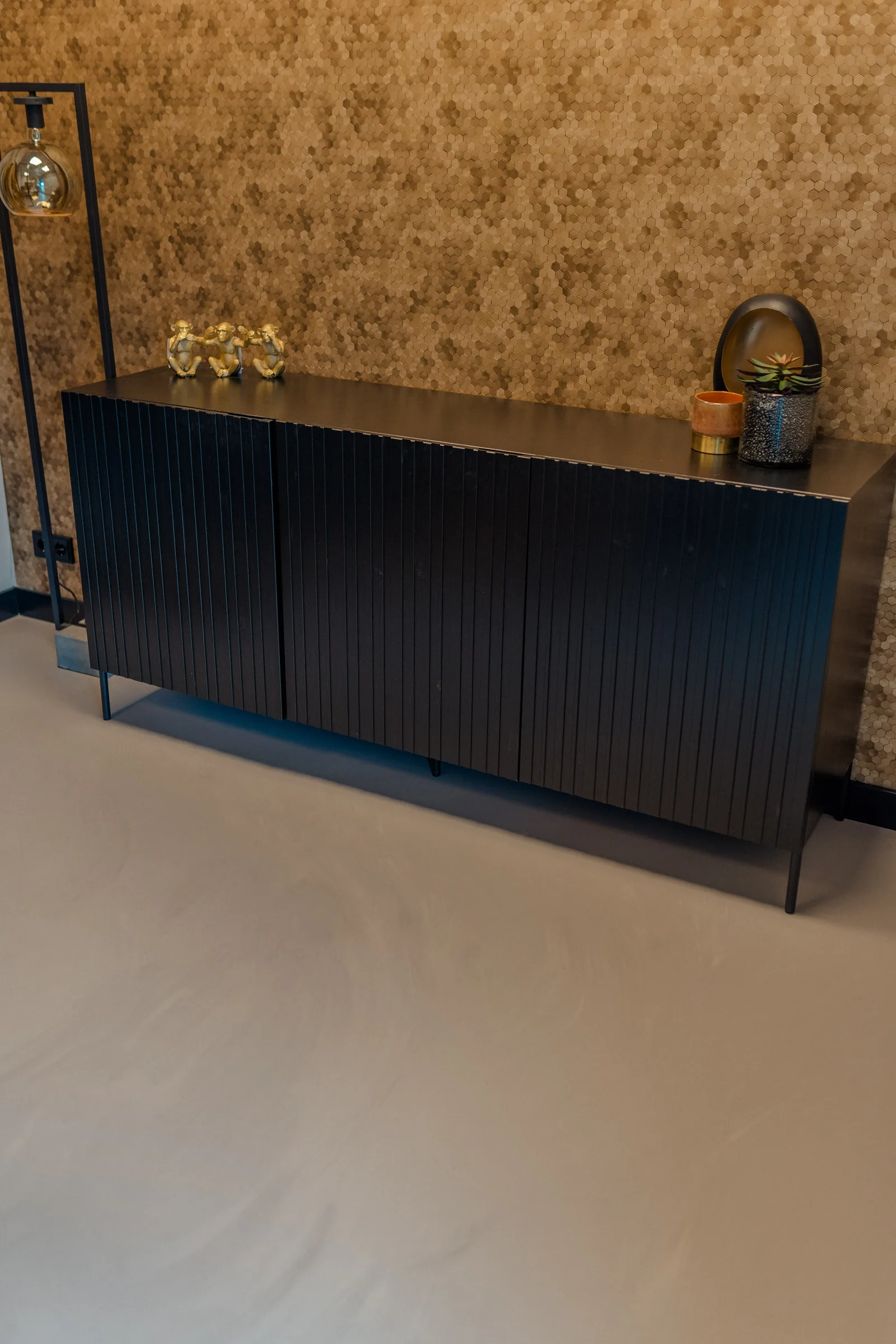Betonlook gietvloer bij een zwart dressoir en gouden accessoires in een showroom