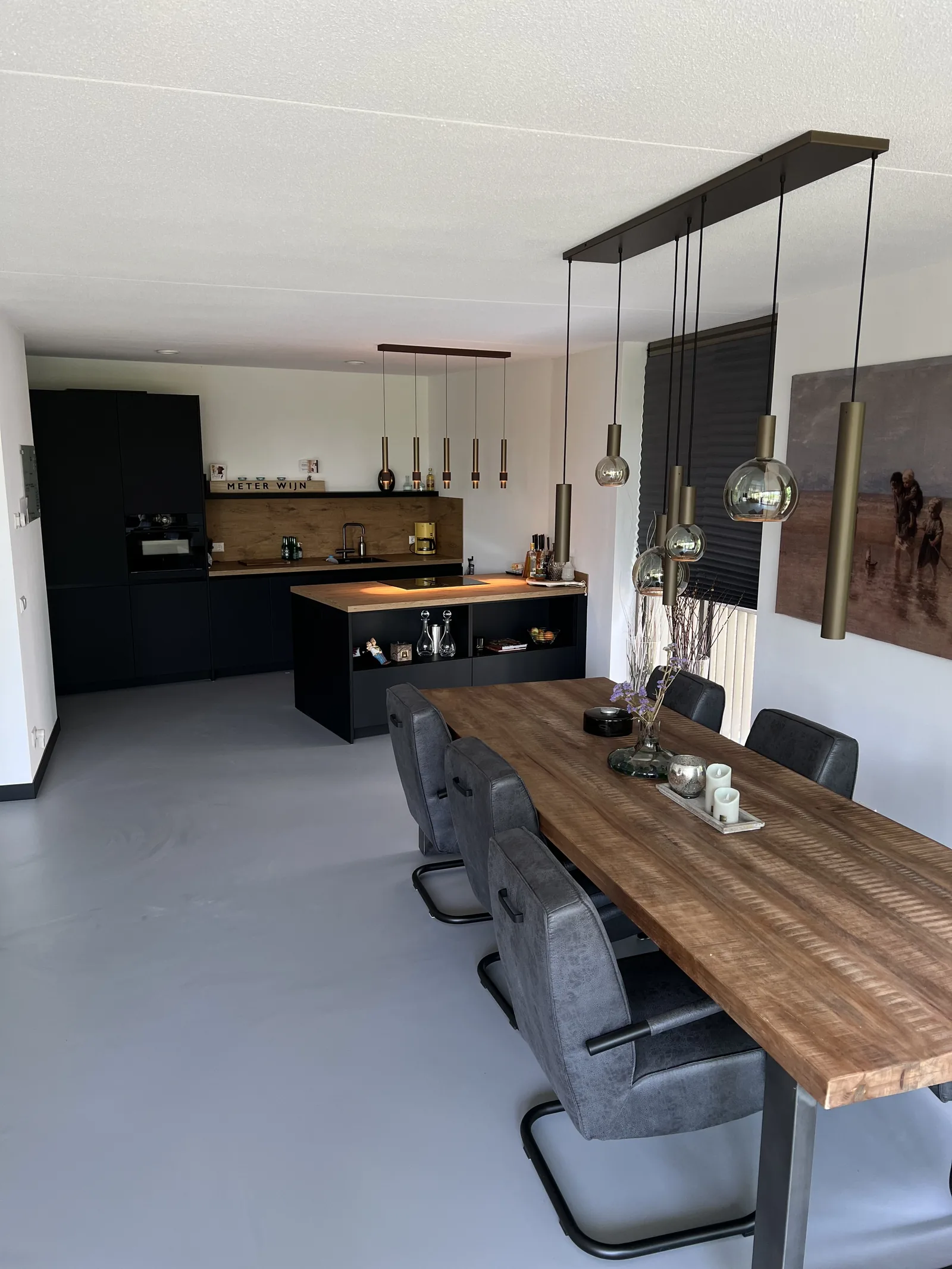 Betonlook gietvloer in een eetkamer met houten tafel, zwarte keuken en hanglampen