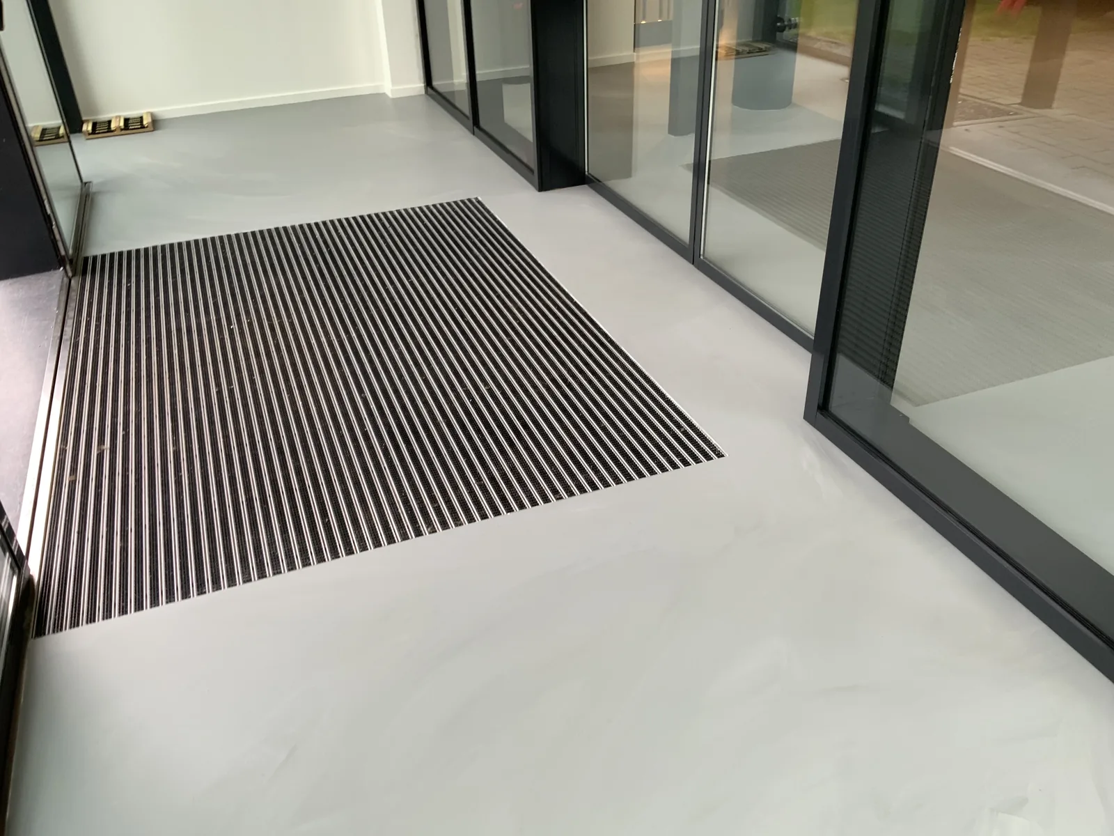 Betonlook gietvloer met ingelegde schoonloopmat bij een glazen entree