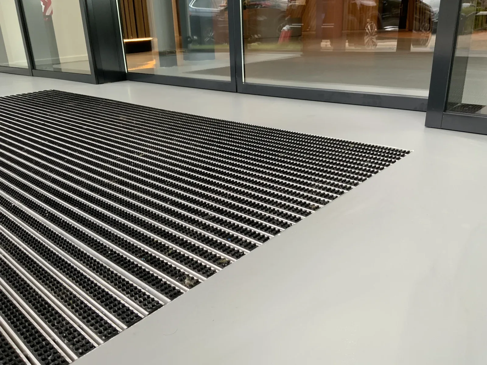 Aluminium schoonloopmat vlak ingelegd in de Comforpur 635 Betonlook gietvloer bij een entree met glazen pui