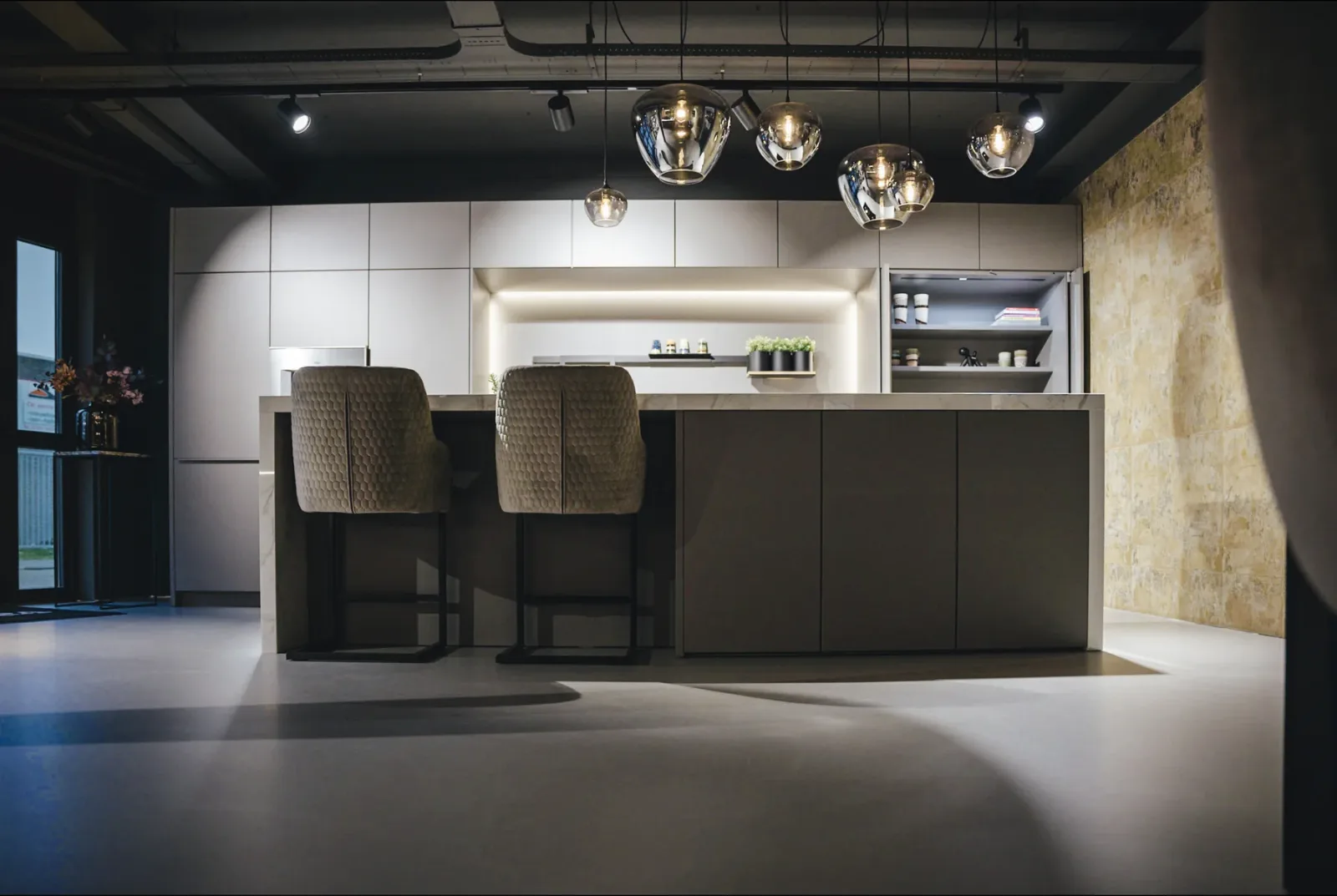 Comforpur 635 Betonlook gietvloer in een keukenshowroom met kookeiland, barkrukken en hanglampen