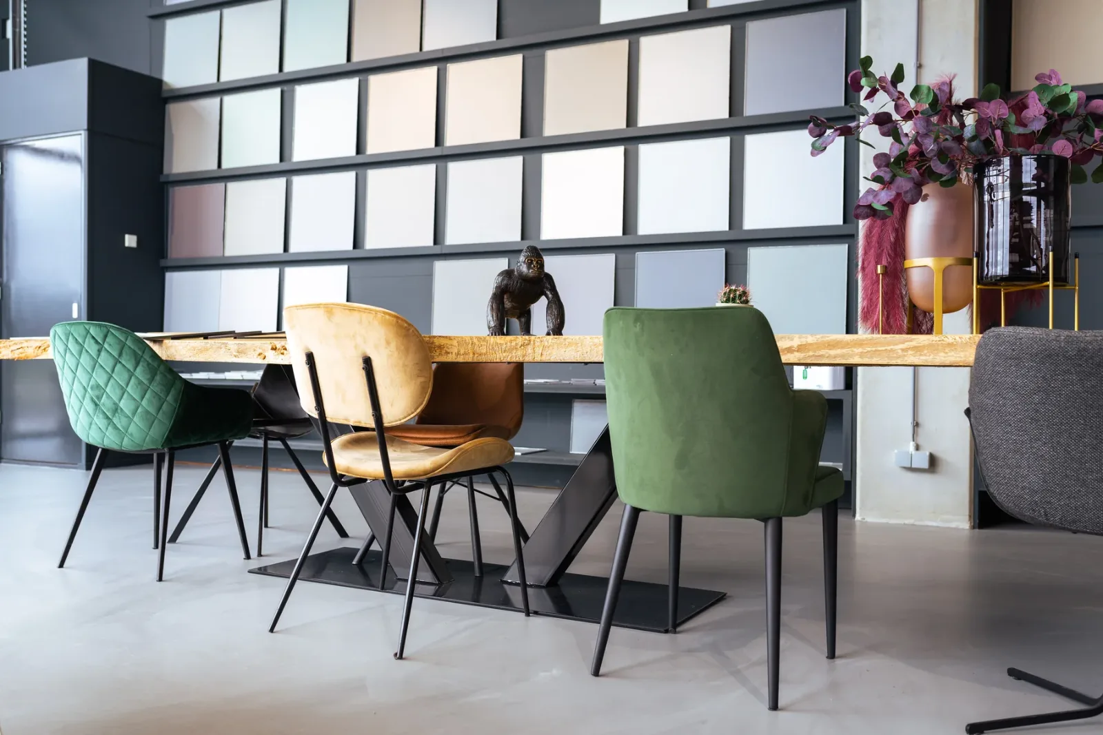 Comforpur 635 Betonlook gietvloer in een showroom met kleurstalenwand en een lange houten tafel met velours stoelen