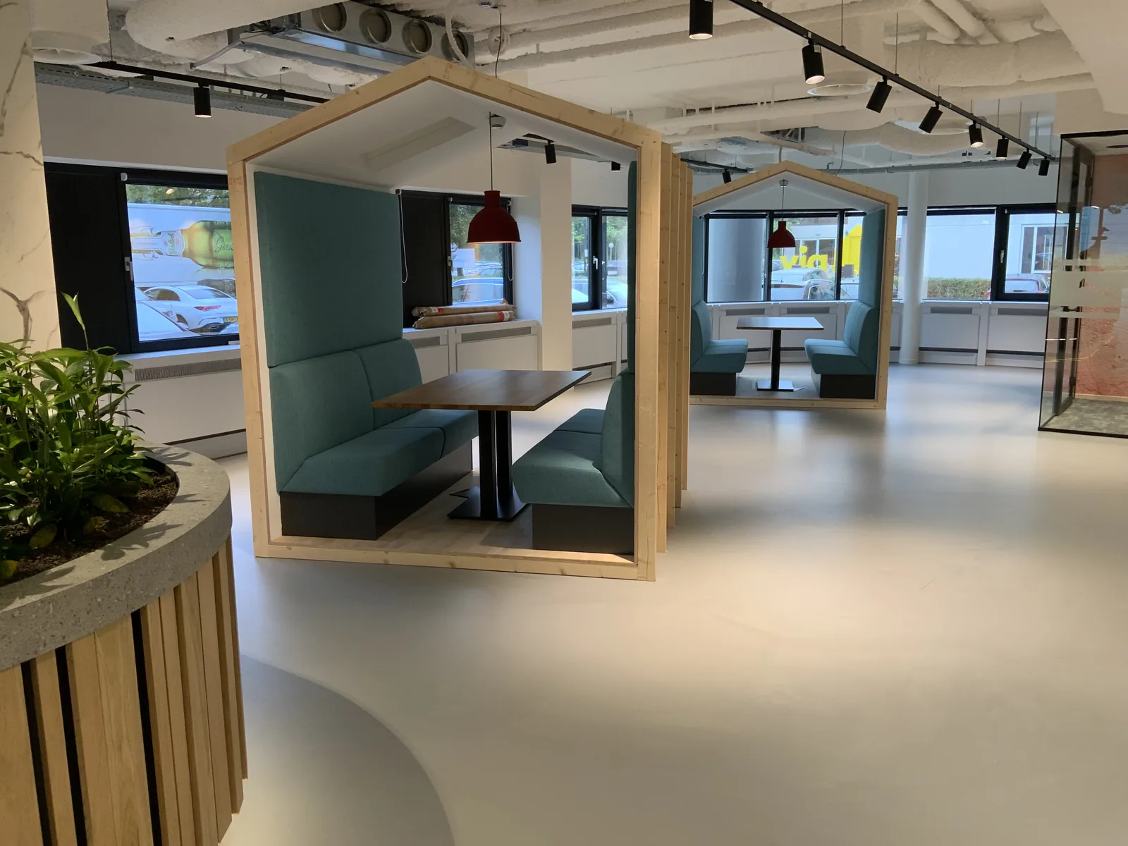 Lichte betonlook gietvloer in een kantoortuin met houten overleghokjes en groen