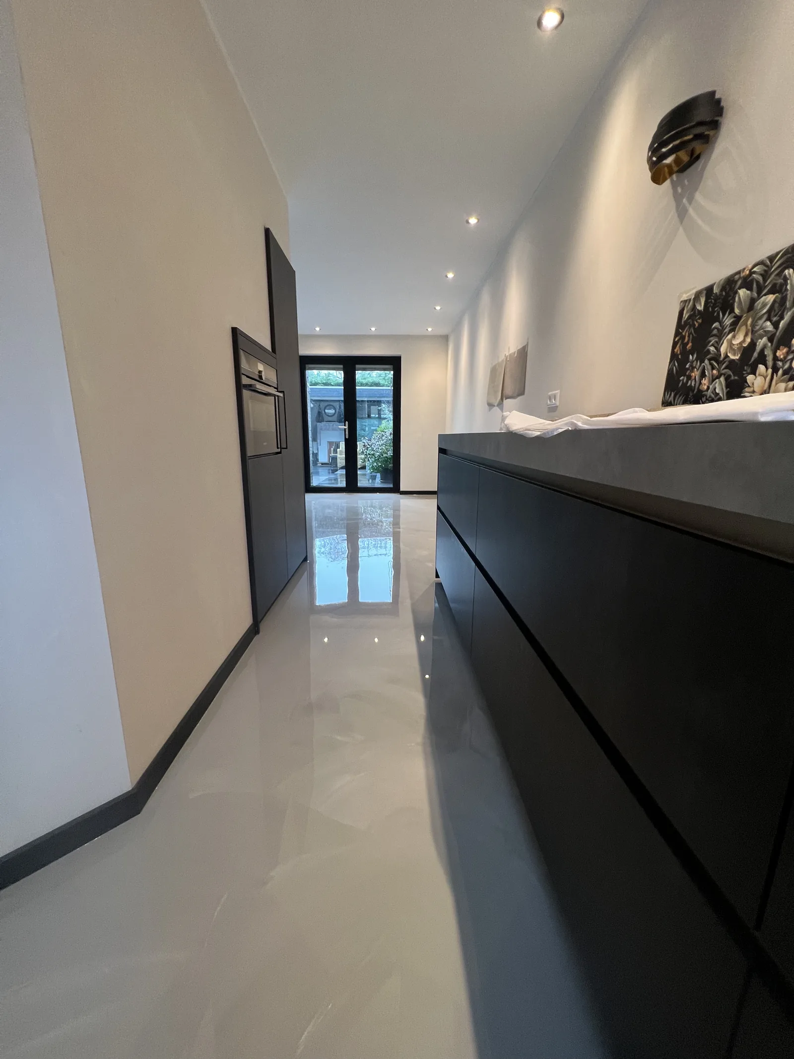 Betonlook gietvloer in een moderne keuken met donker kookeiland en inbouwoven
