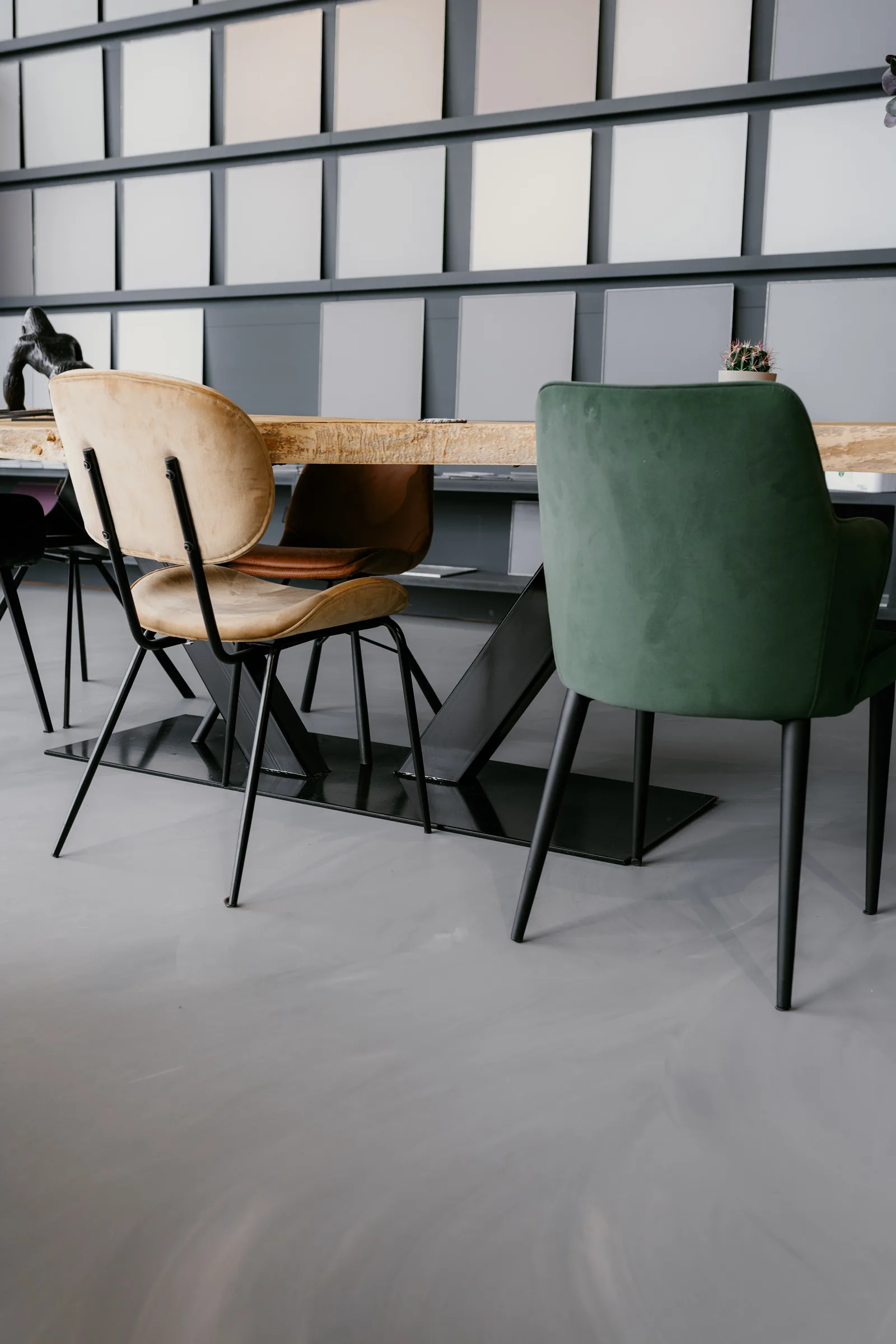 Betonlook gietvloer in een showroom met kleurstalenwand en velours stoelen