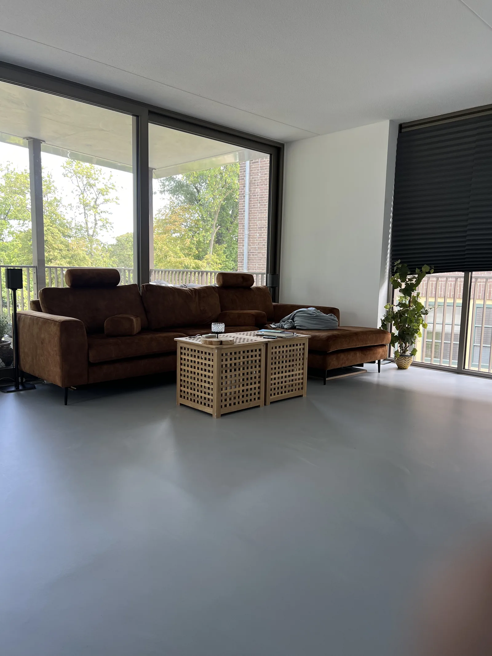 Comforpur 635 Betonlook gietvloer in een woonkamer met bruine bank en uitzicht op de tuin