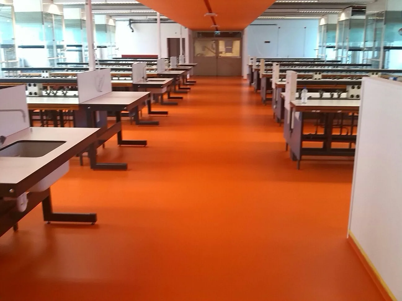 Oranje gietvloer in een kantoorruimte met werktafels en groene wanden