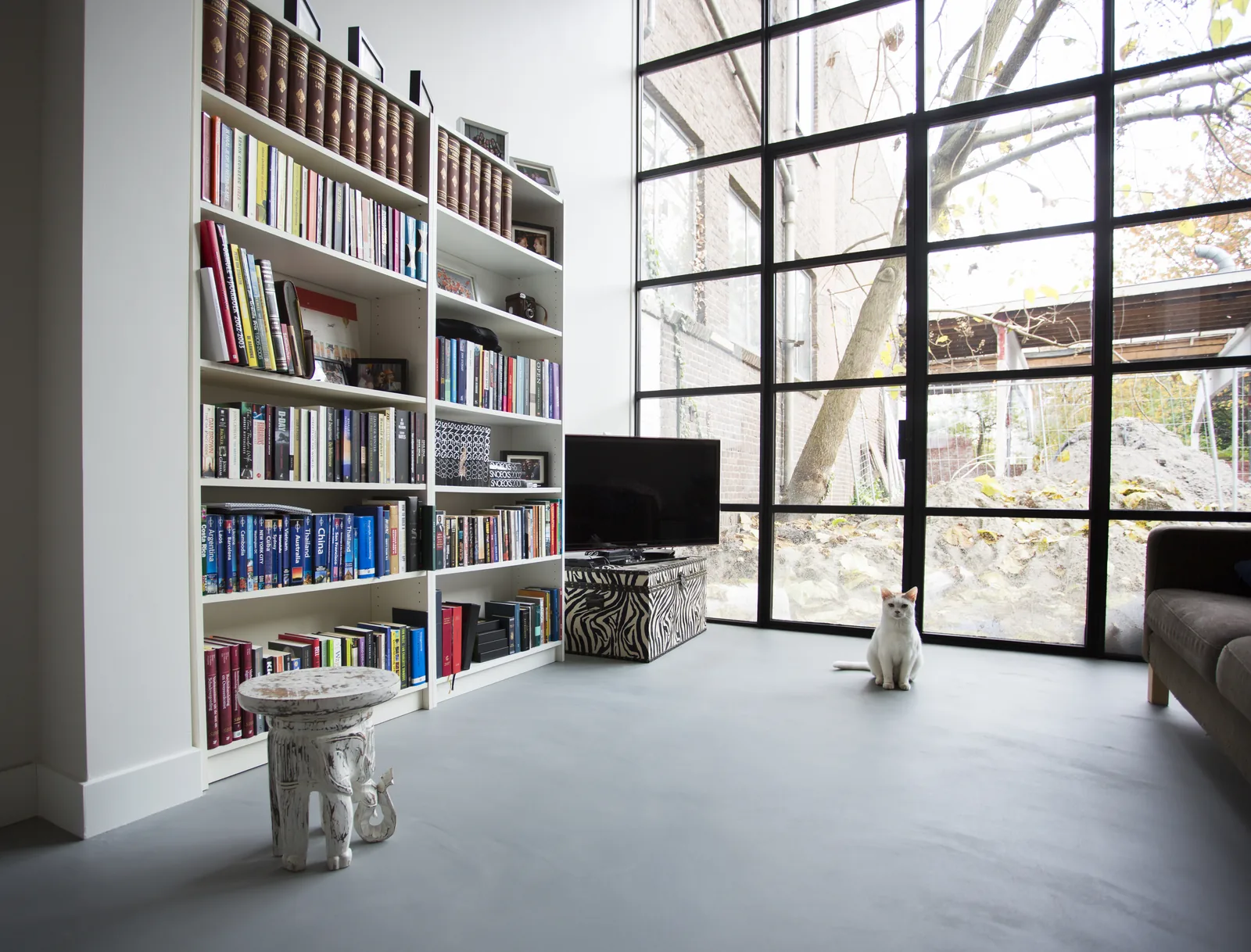 Lichte gietvloer in een woonkamer met boekenkast en stalen deuren