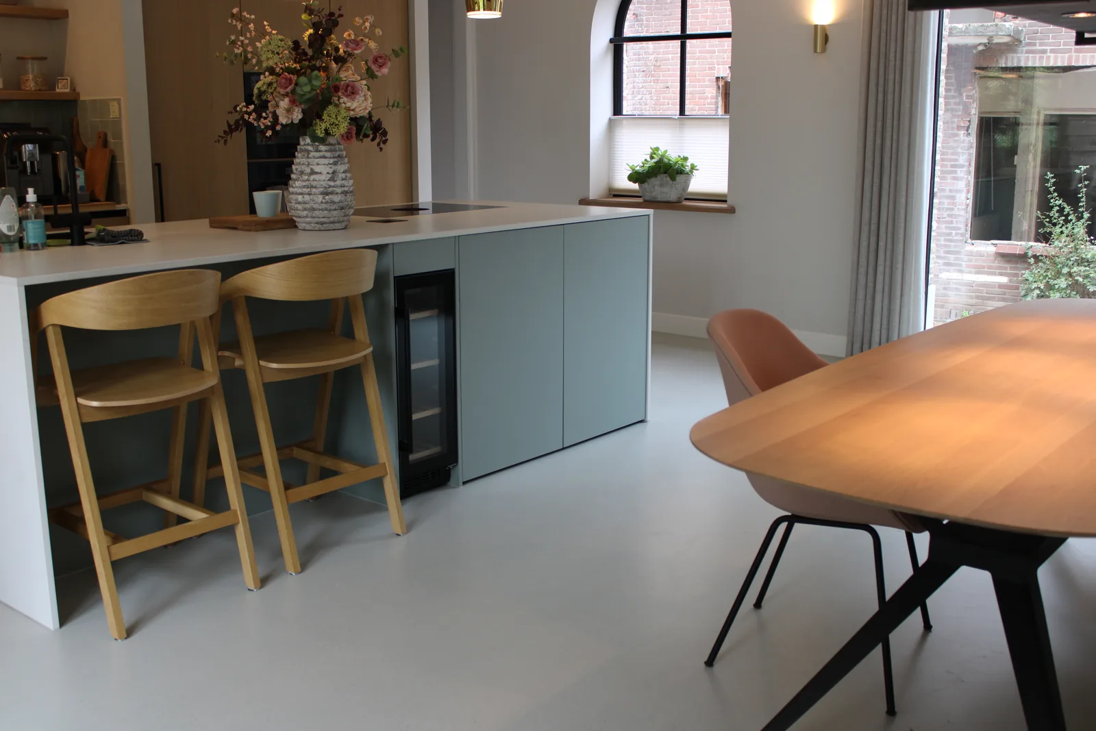 Gietvloer bij een houten eettafel en keukenbar met barkrukken