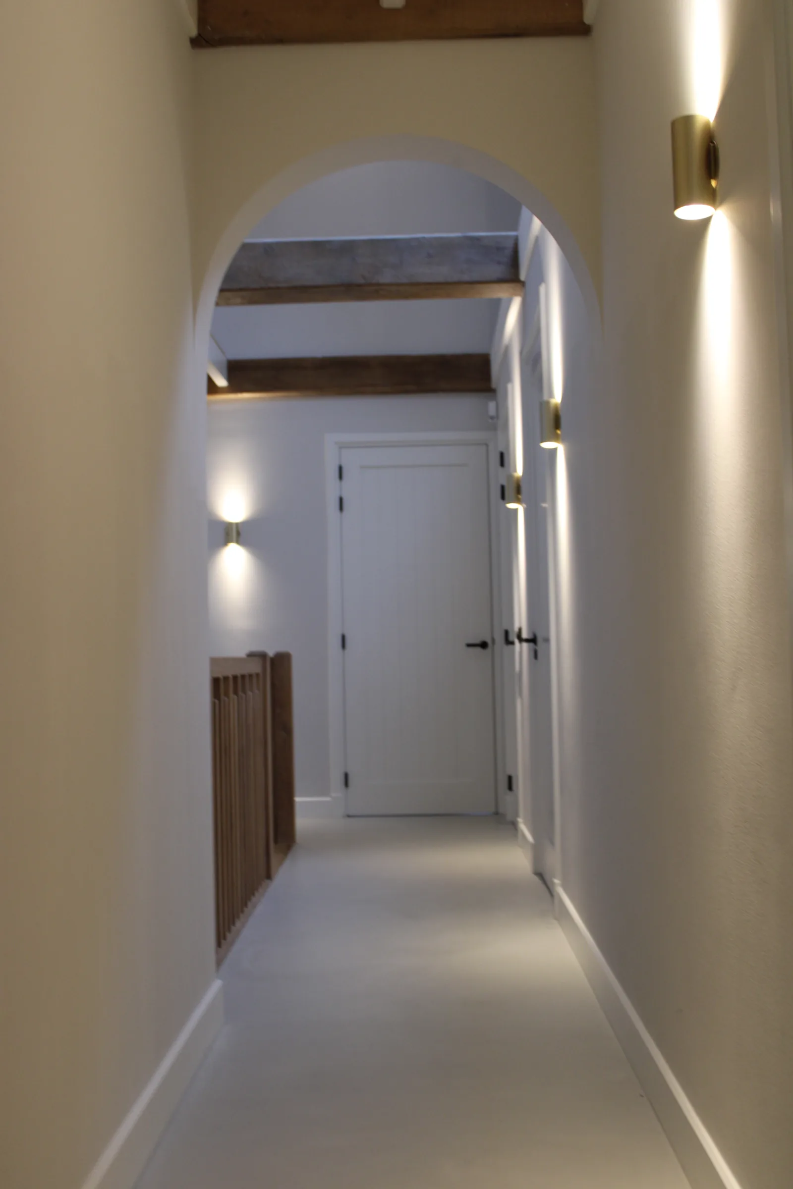 Gietvloer in een gang met witte deuren en wandverlichting